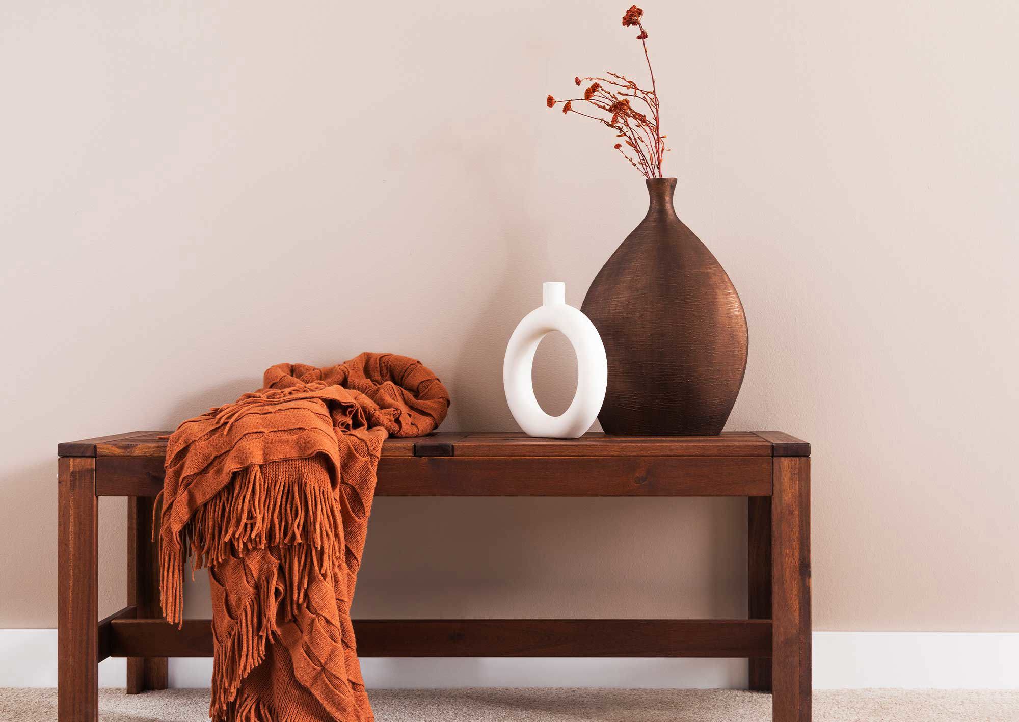 Bänk framför en vägg i naturnära ton med vaser på