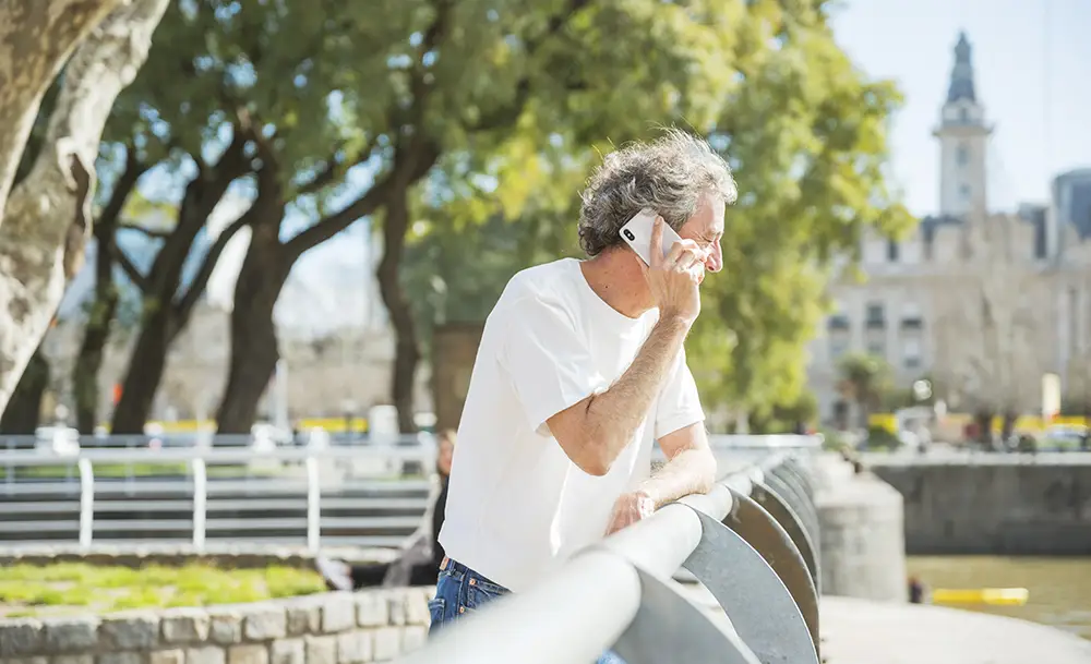 senior man som står på en bro och pratar i telefon