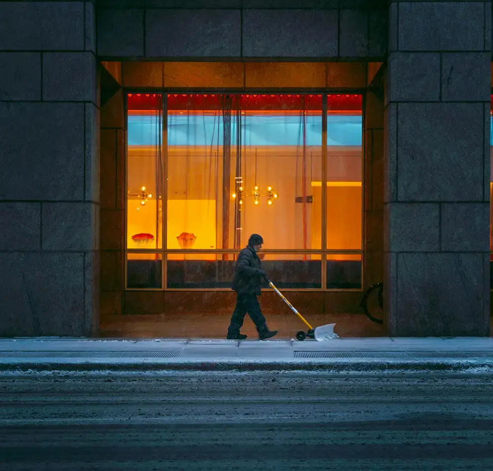 man som skyfflar gatan framför ett fönster