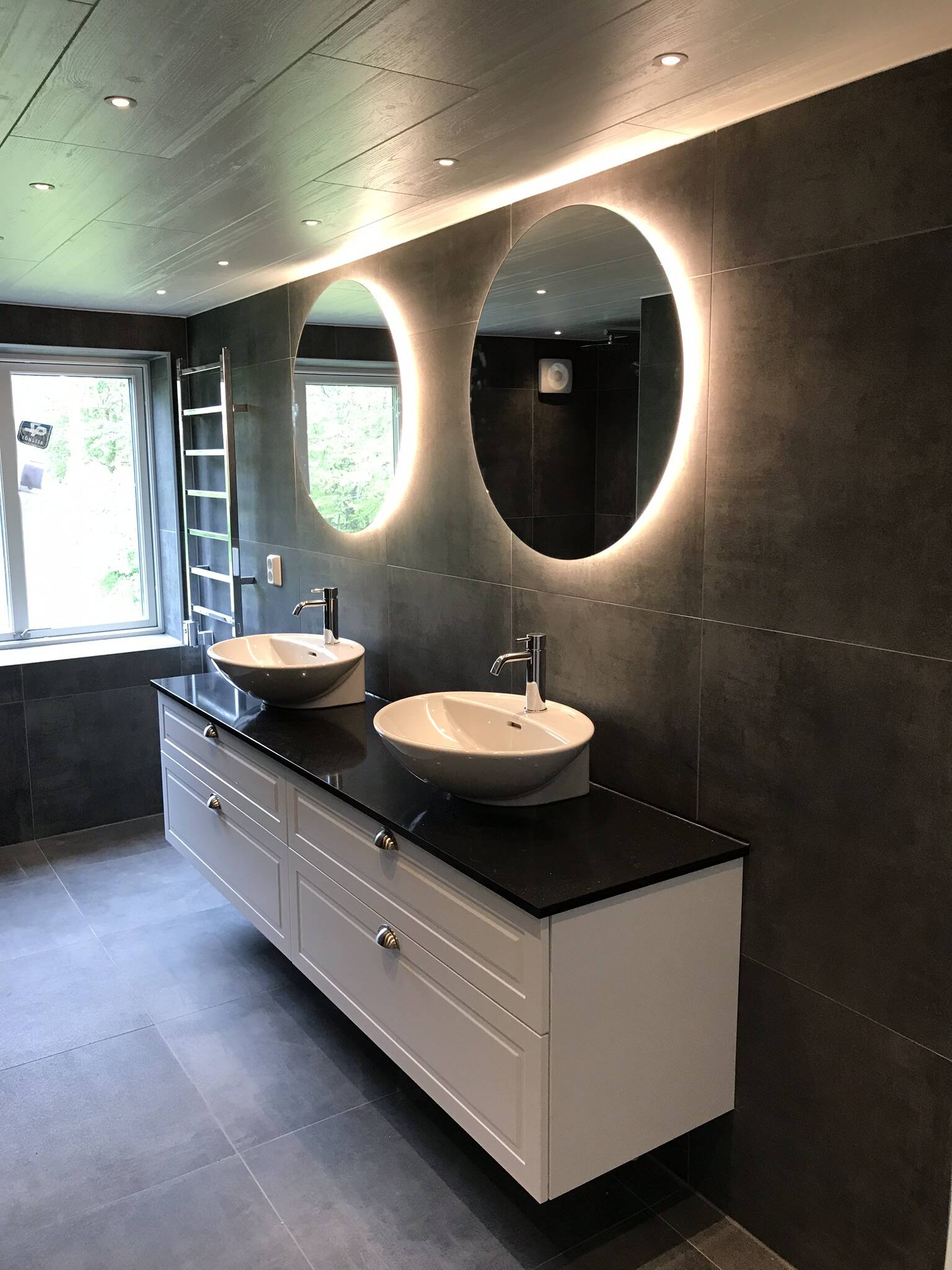 Ett nybyggt, fräscht badrum med svarta väggar och ljus bakom speglarna