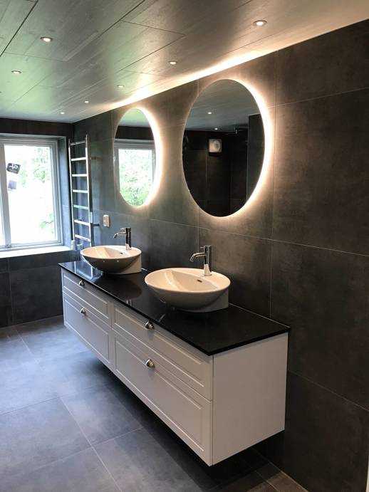 Ett nybyggt, fräscht badrum med svarta väggar och ljus bakom speglarna