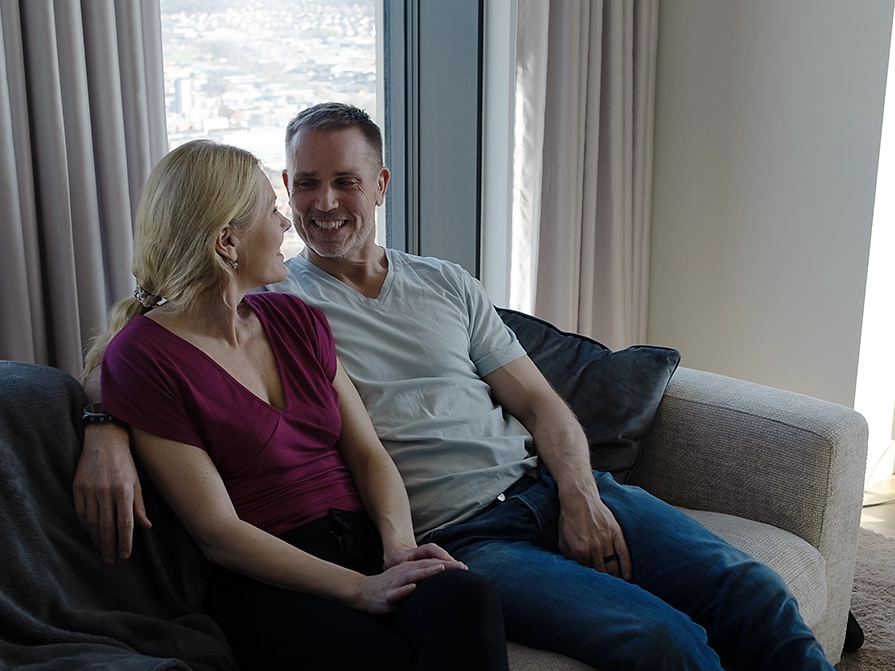 Annika och Johan sitter tillsammans i en soffa och ler mot varandra