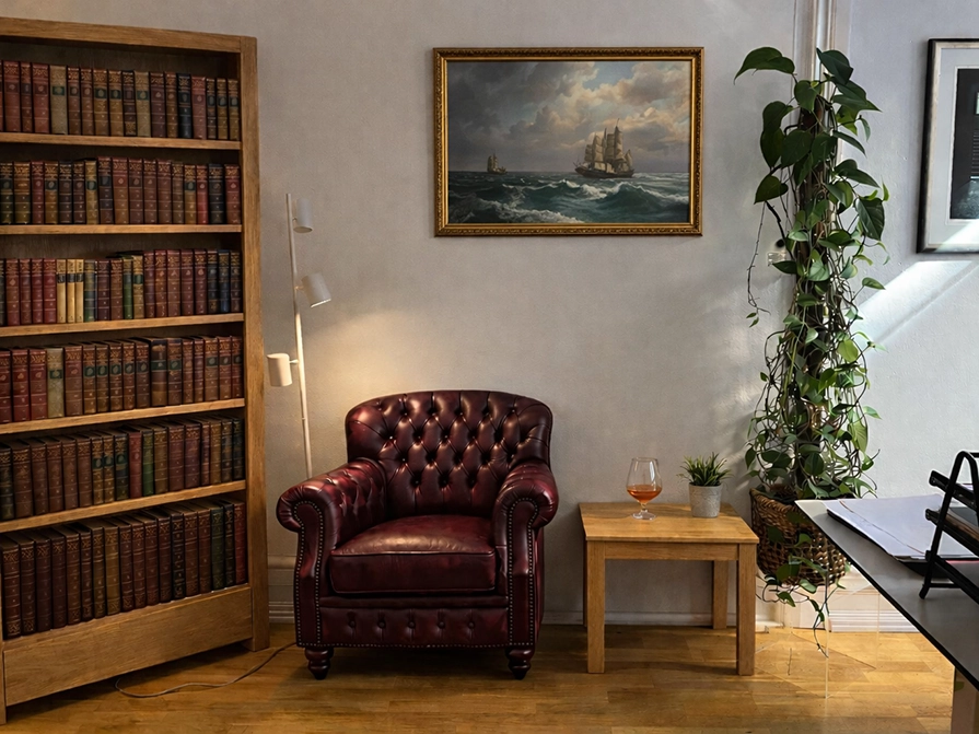 läshörna i ett kontor med en bokhylla, en röd läderfåtölj och ett bord