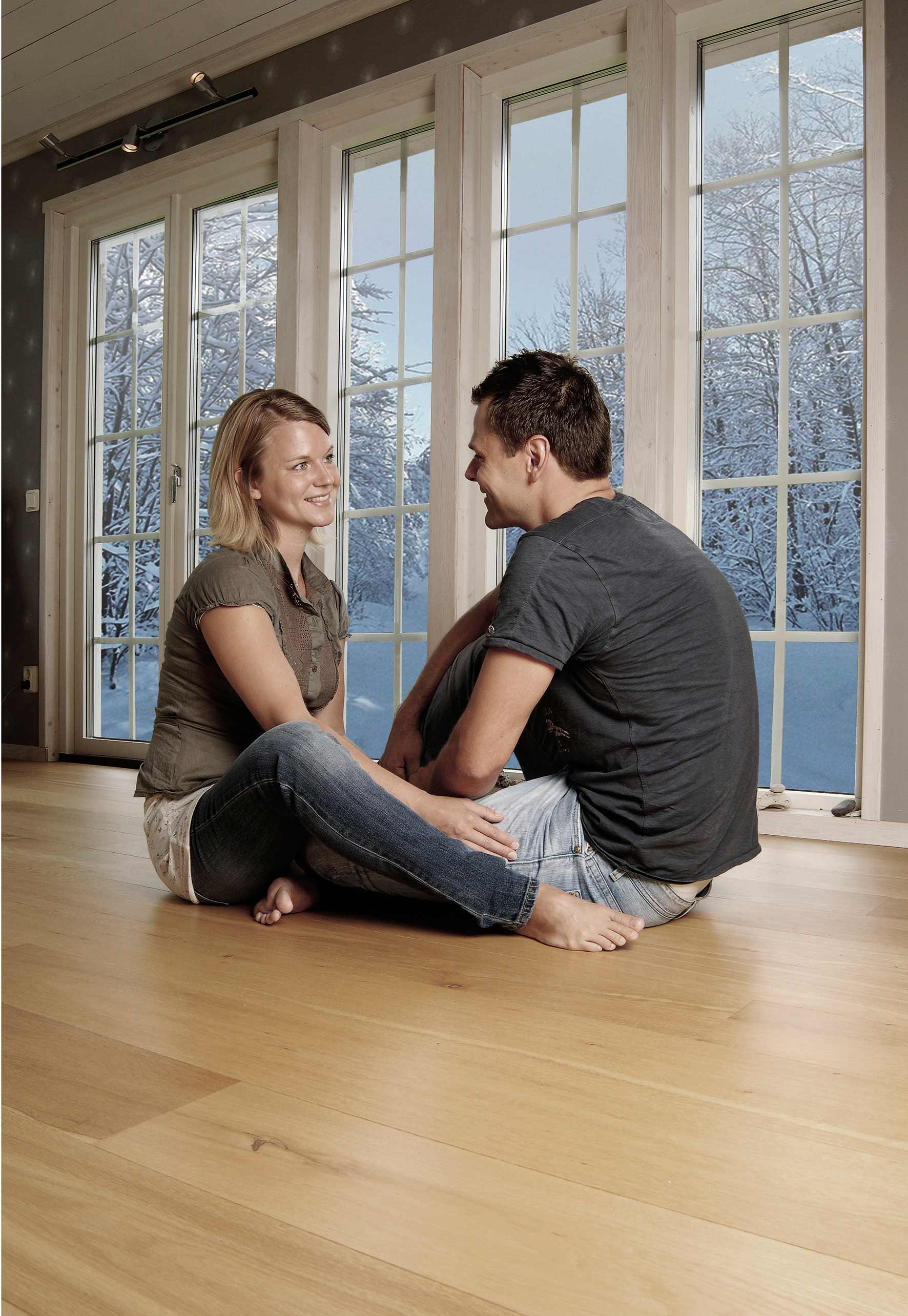 kvinna och man som sitter på parkettgolv, stora fönster i bakgrunden