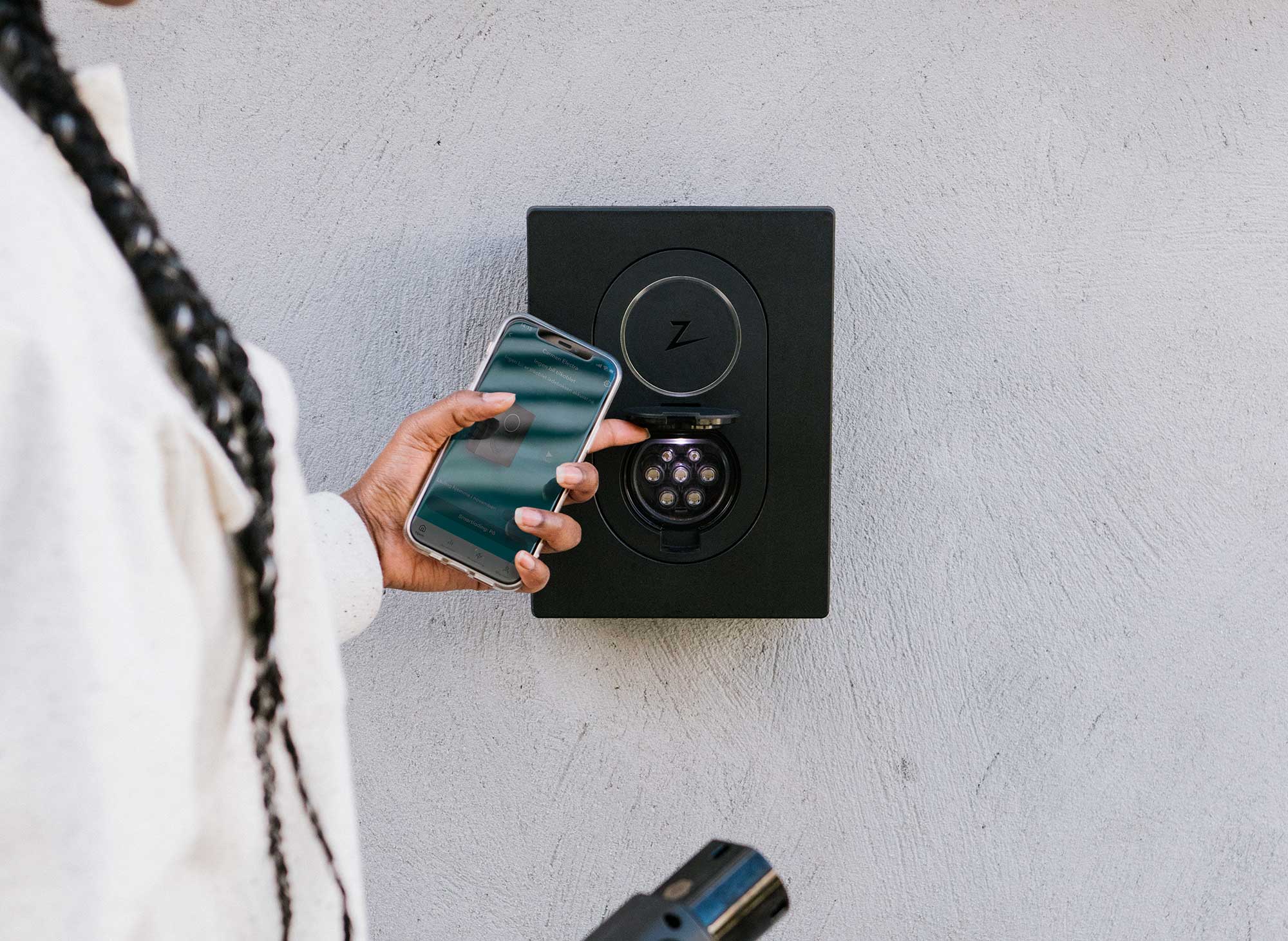 Laddbox till elbil, kvinna står med telefon,