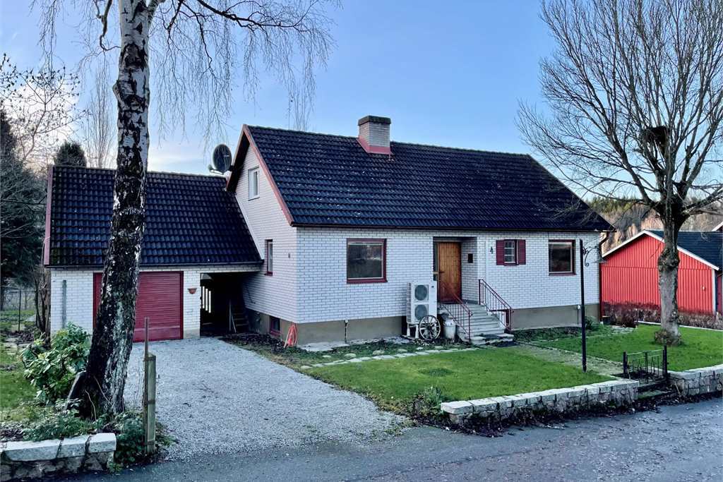 gråvit tegelvilla med svart tak och gräsmatta framför